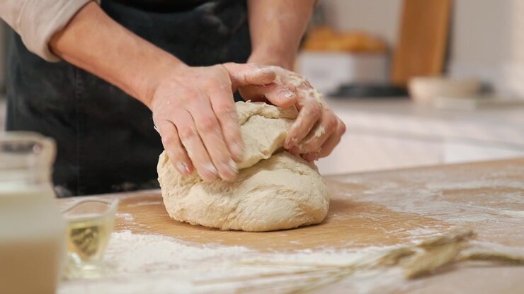 Close-up of Hands Kneading Fresh Dough on a Floured Wooden Table