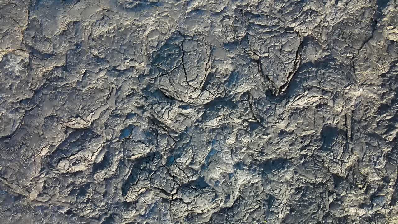 una hipnotizante toma de drones de arriba hacia abajo capturando la cautivadora belleza de la lava seca mientras brilla en el sol de la mañana, revelando la intrincada textura y los patrones de este terreno volcánico
