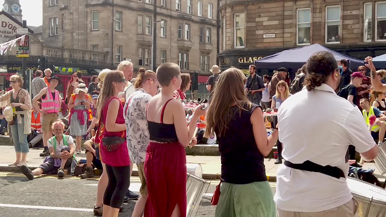 Slow-motion of Extinction Rebellion protesters playing music in front of a small crowd.