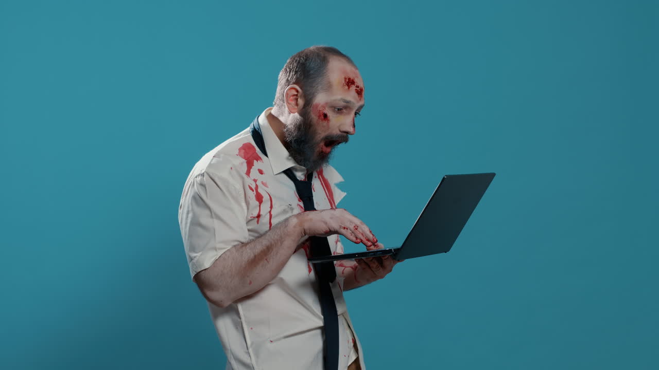 Dirty spooky zombie with open bloody wounds and scars using modern laptop
