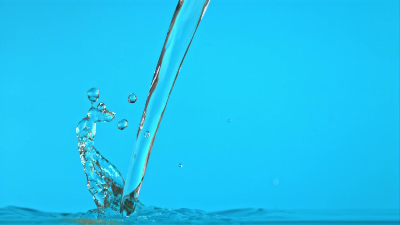 Clear Water Pouring and Splashing on a Blue Background in Slow Motion