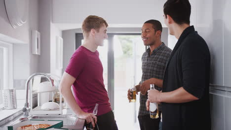 group of male college students in shared house kitchen drinking beer and eating pizza together