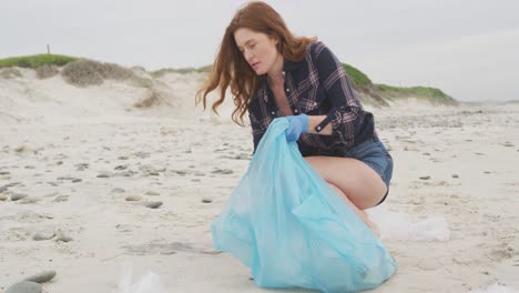 caucasian woman wearing latex gloves collecting rubbish from the beach looking ahead