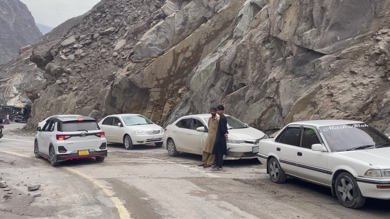 A line of cars parked on the winding Gilgit Skardu Road as drivers experience a significant landslide. Rugged mountain landscape with travelers facing delays.
