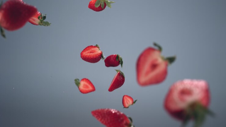 SUPER SLOW MOTION shot of fresh sliced strawberries flying against bright background, water drops splash. Shot with high speed camera.