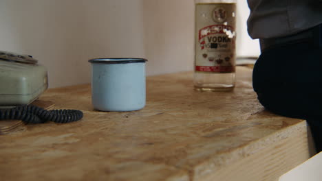 man with a cup and vodka bottle on a wooden table