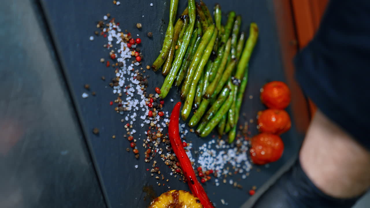 Cook puts the fried vegetables on the black charcuterie board. Serving the dish. Close up. Vertical view.