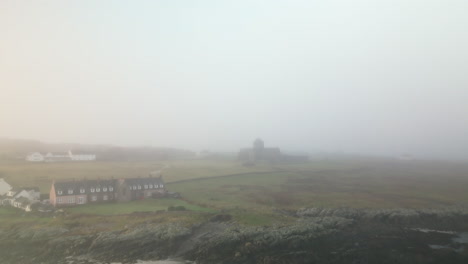 upward linear aerial of foggy landscape with house and monastery in distance