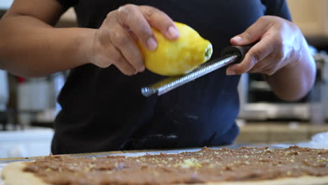 zesting a whole lemon over dough and cinnamon filling to roll into tasty, sweet buns - side view in slow motion