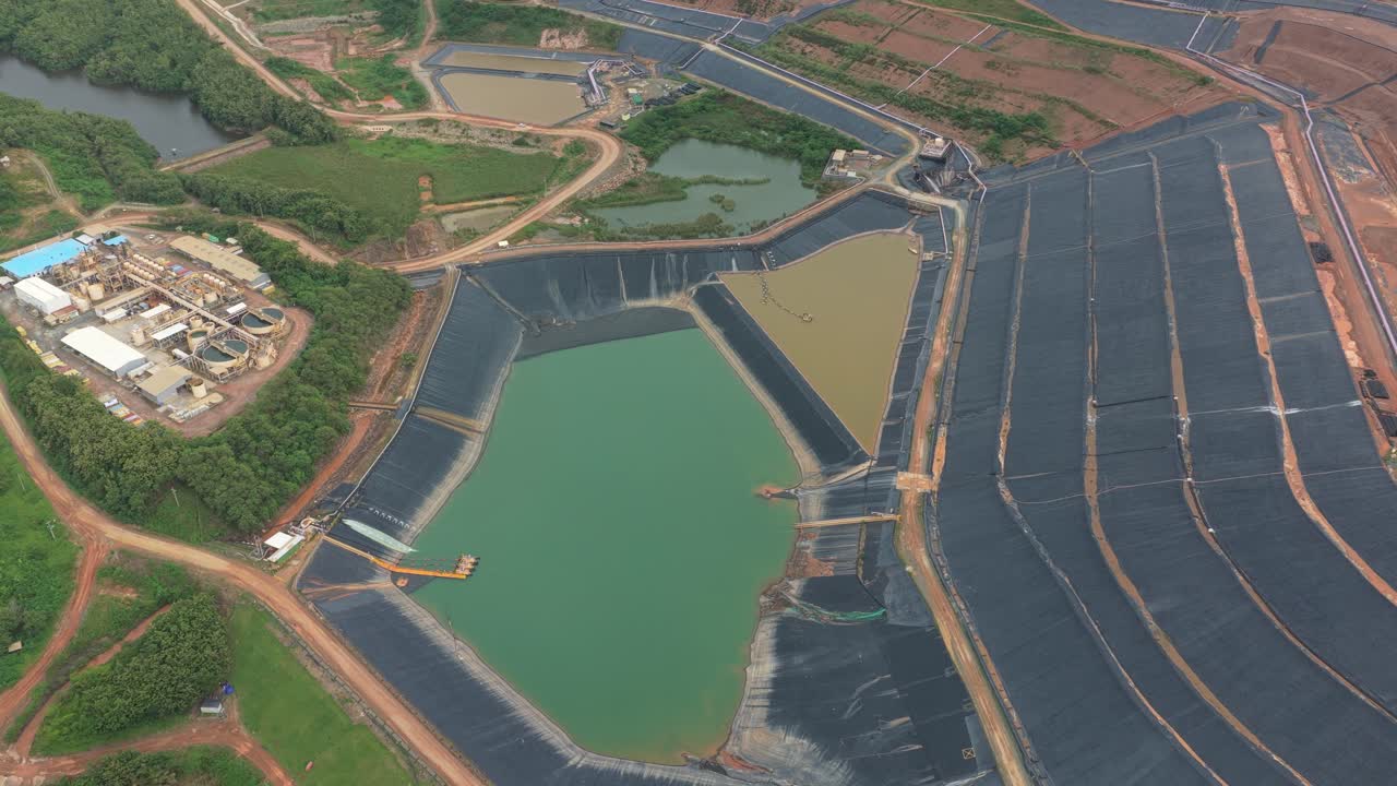 Overhead perspective showing a large industrial mining complex with tailing dams, water treatment ponds, and surrounding green landscape