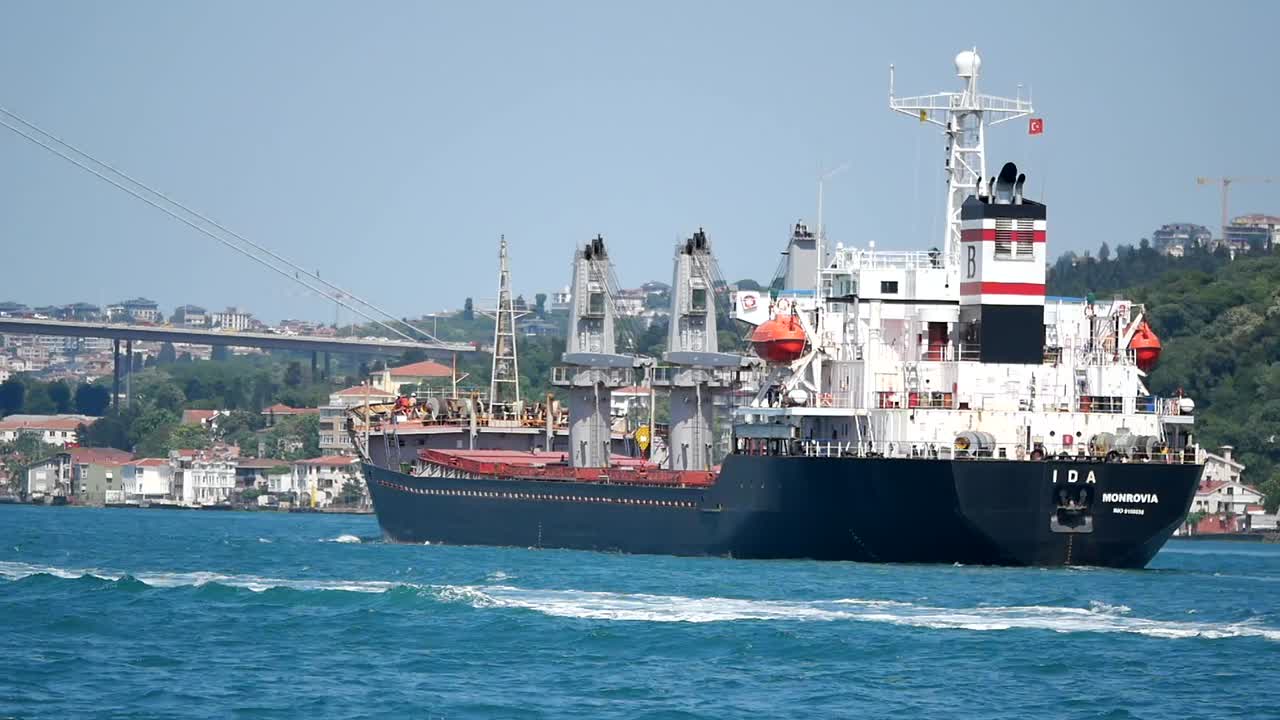 A cargo ship sailing on a blue body of water with a bridge and city in the background