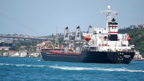 a cargo ship sailing on a blue body of water with a bridge and city in the background