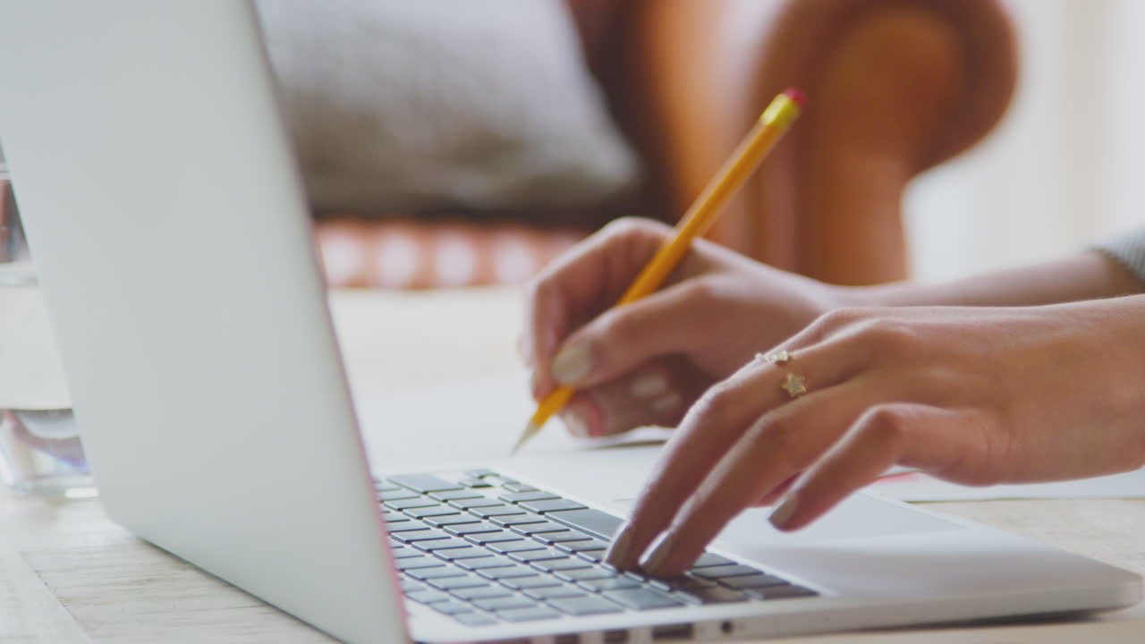 un primer plano de una mujer trabajando desde casa en una silla escribiendo en el teclado de una computadora portátil