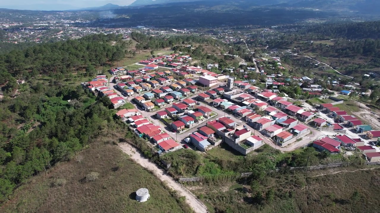 Una toma de dron a gran altitud captura un denso barrio residencial en América Latina, con aproximadamente 150 casas con techos de zinc rojos rodeadas de exuberante bosque.