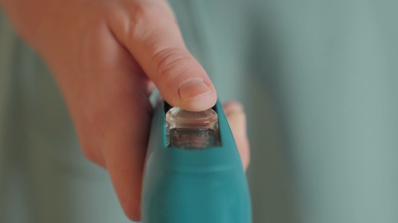 Closeup fingertip on steam cleaner button, homeowner adjusts delicate setting for house cleaning, teal handheld steamer, soft shallow focus, calm domestic mood, careful press sequence, precise
