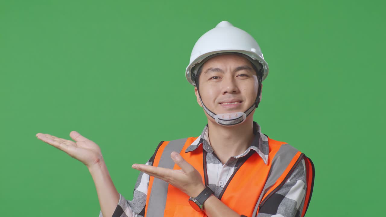 Close Up Of Asian Male Engineer With Safety Helmet Smiling And Pointing To Side While Standing In The Green Screen Background Studio