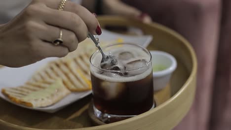 Young-woman-whisk-with-metal-spoon-to-an-iced-tea-in-a-glass-cup