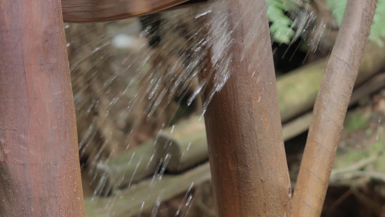 Dettaglio ravvicinato di acqua fresca che schizza e scorre attraverso i raggi e le pale di legno rustiche di una ruota idraulica tradizionale.