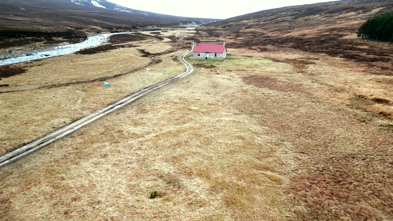 A drone flies away from a the recently renovated Red House Bothy in the Scottish highlands as a person walks out of the front door