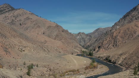 Drone-footage-following-a-backcountry-single-engine-plane-over-a-river,-surrounded-by-mountains,-and-landing-on-a-remote-landing-strip-in-the-Frank-Church-River-of-No-Return-Wilderness