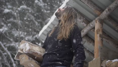 hombre brutal sosteniendo leña y admirando los copos de nieve que caen