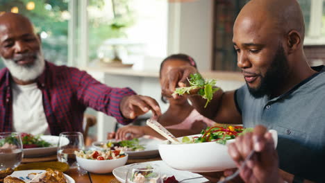 close up of multi-generation family sitting around table serving food for meal at home together