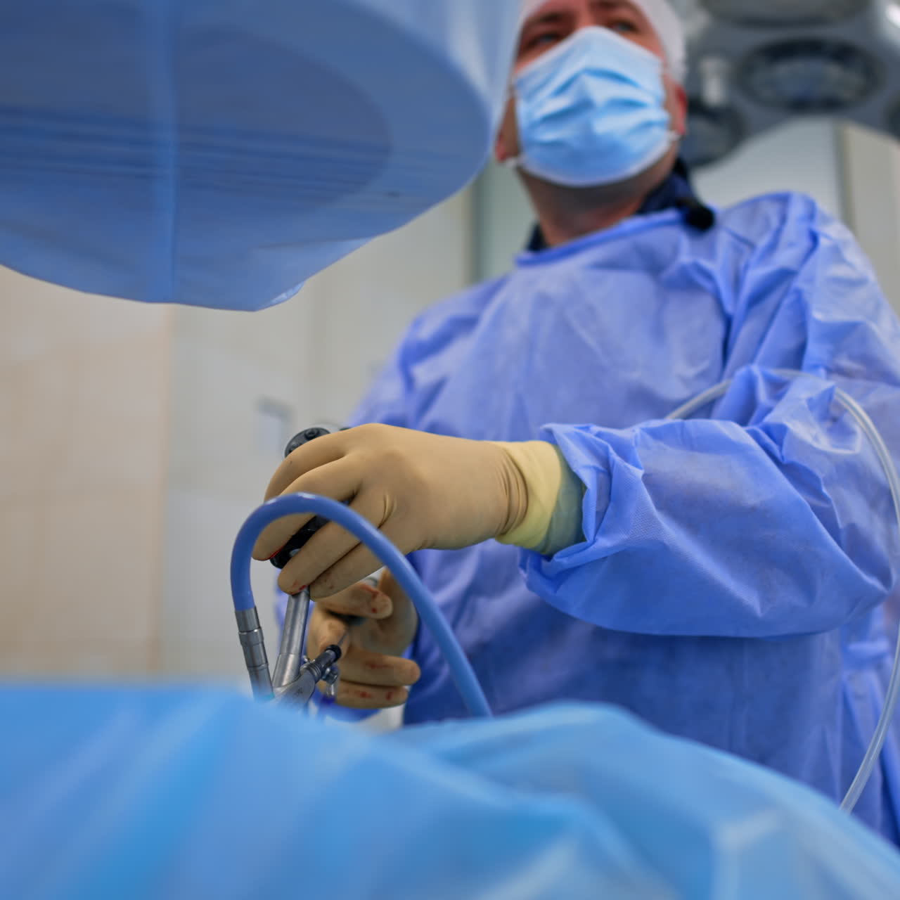 Uniformed male surgeon moving slowly the endoscopic device performing surgery. Low angle view on the doctor operating the patient.