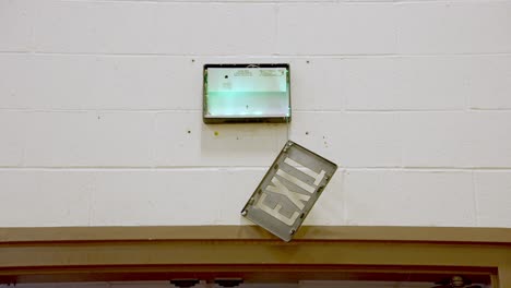 handheld shot of damaged exit sign hanging on top of gym door