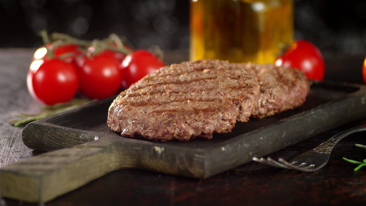 Fried burger meat on a cutting board with tomatoes rotates.