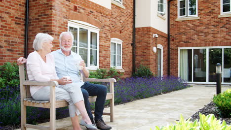 retired couple sitting on bench with hot drink in assisted living facility