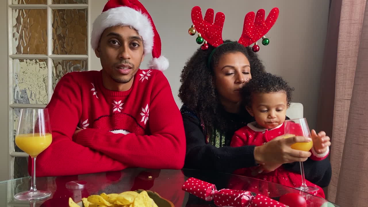 Giovani genitori con un bambino piccolo in una videochiamata di Natale che ascoltano e parlano alla telecamera
