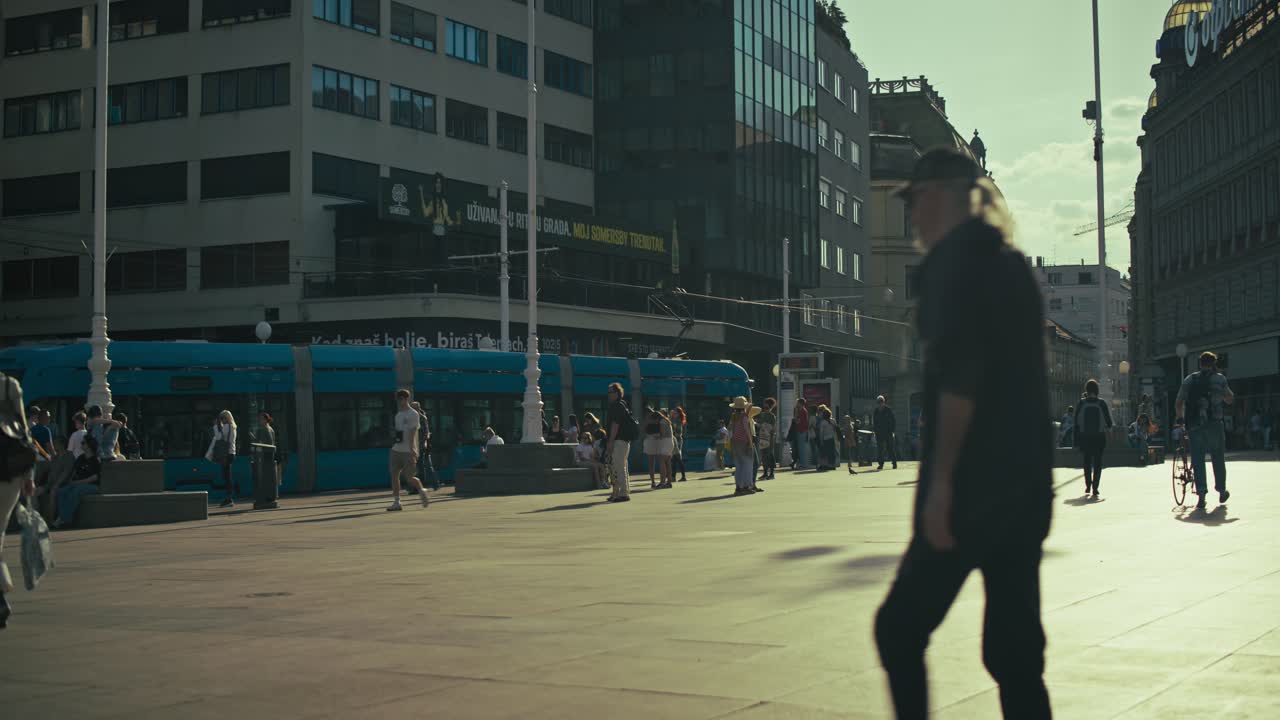 Pedestrians walk through Josip Jelačić Square, Zagreb, with trams and modern buildings in the background