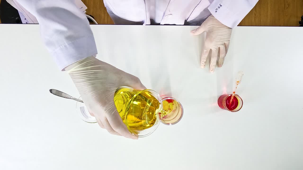 Hands in gloves mix liquids in a lab setting, creating a vibrant lava lamp effect with food coloring