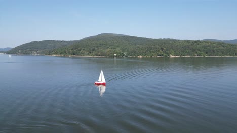 barco de vela en el lago tranquilo en las montañas beskid, rodeado de vegetación durante un caluroso día de verano - vista aérea de dron 4k