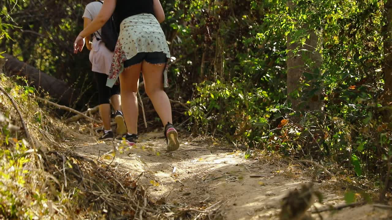 Vista trasera de mujeres caminando cuesta arriba por un estrecho sendero de tierra a través de vegetación de selva seca en Yelapa, Jalisco, México