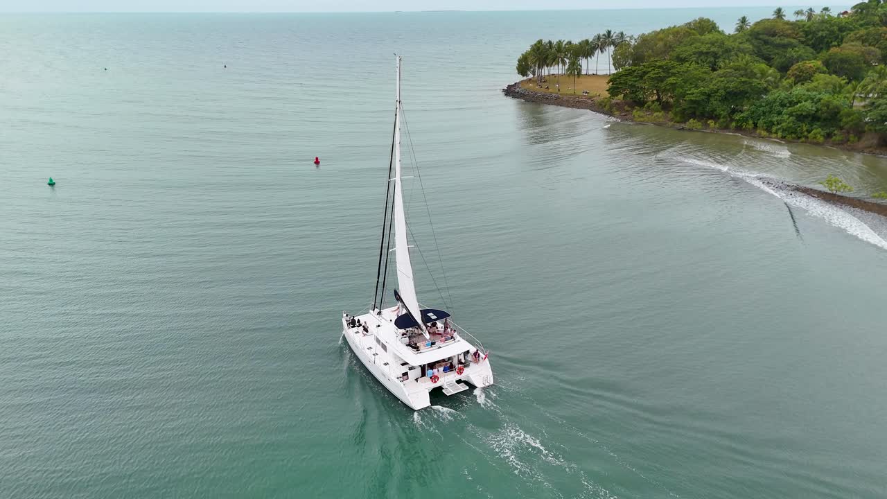 Drone captures a catamaran sailing along the serene waters near lush coastline in Port Douglas, Australia