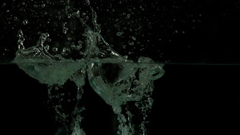 three limes plunging into water on black background