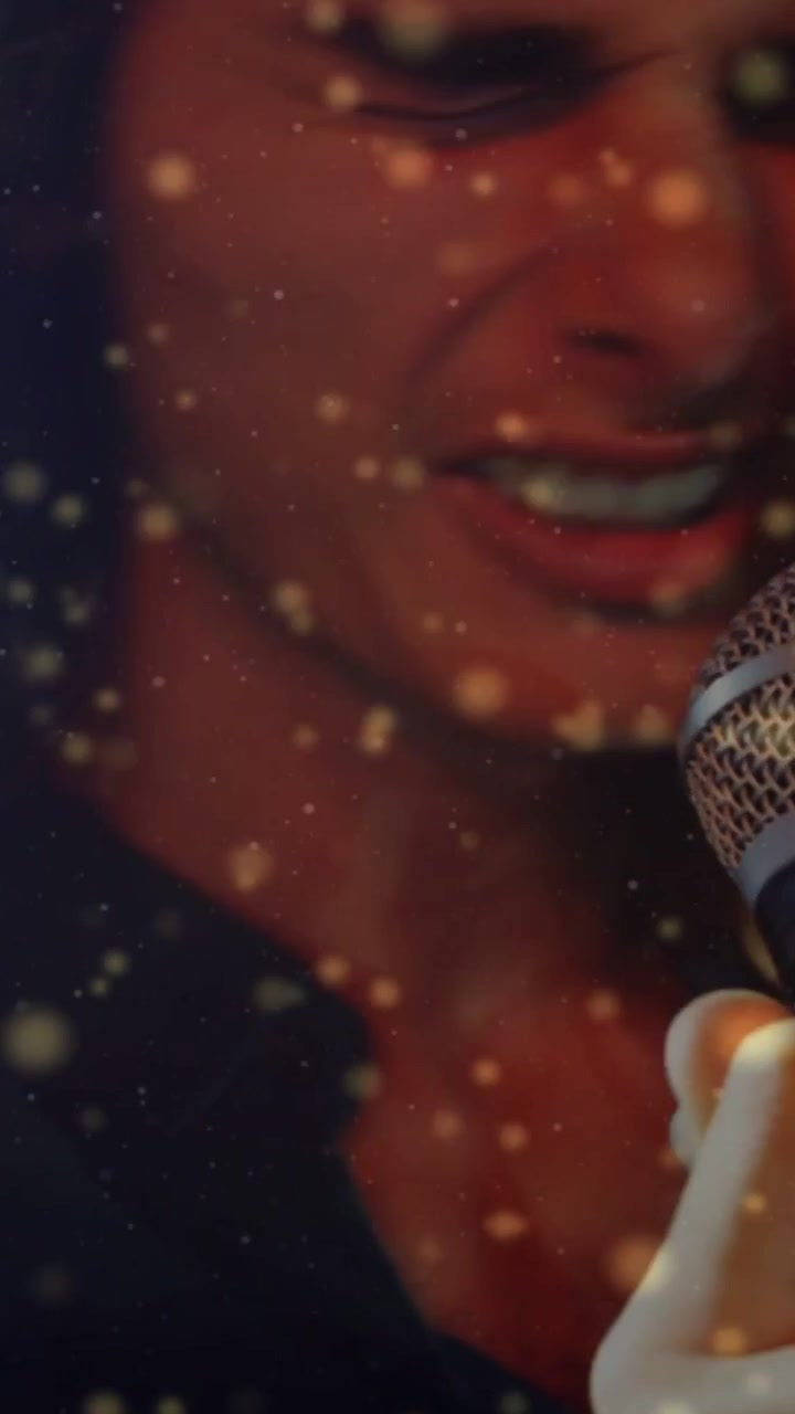 Vertical video: Male singer gripping mic, singing emotionally while hair flying amid golden dust