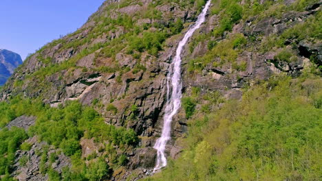 a waterfall flowing down a cliff near flam, norway - pull back aerial reveal