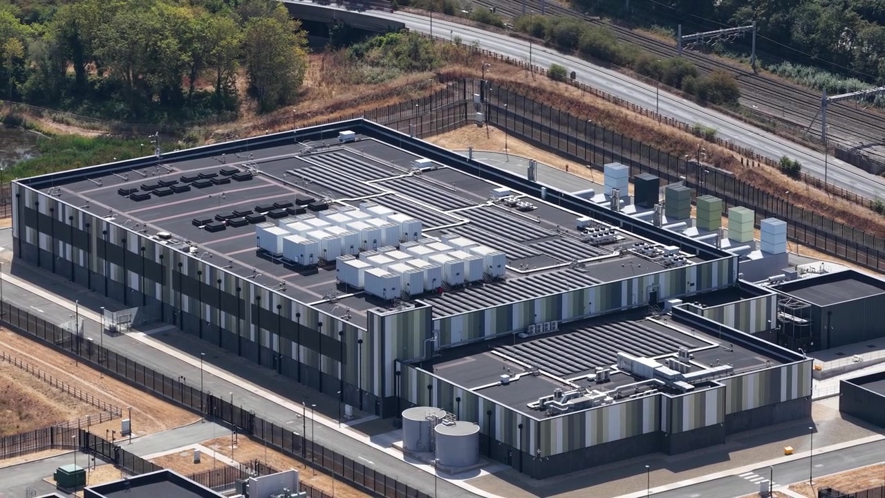 Dronebillede fra høj vinkel af et massivt datacenteranlæg med HVAC-køleenheder, transformerstationer og moderne arkitektur, der driver cloud-netværk og AI-systemer