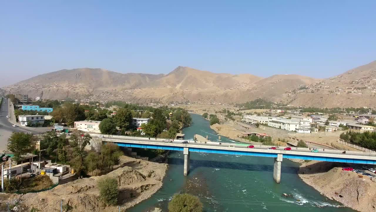 una toma aérea de un puente que cruza un río en un pueblo, con coches que cruzan el puente