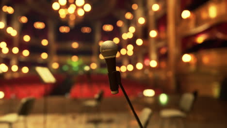 a close-up shot of a microphone on a stand in front of a stage with blurry background.