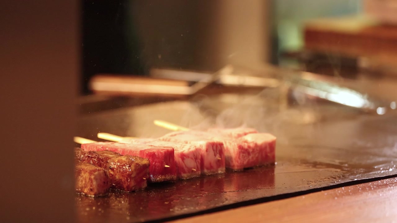 Primo piano di spiedini di manzo Wagyu marmorizzato che cuociono con vapore su una piastra teppanyaki