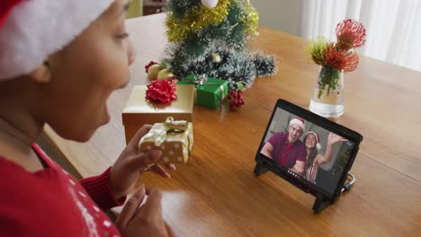 African-american-woman-with-santa-hat-using-tablet-for-christmas-video-call-with-couple-on-screen