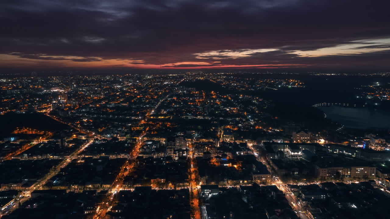 Aerial drone timelapse view of Chisinau at sunset, Moldova. View of city centre with multiple buildings, roads, lake, illumination