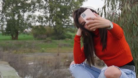 female model taking a break during photo shoot to take some selfies next to river in slow motion