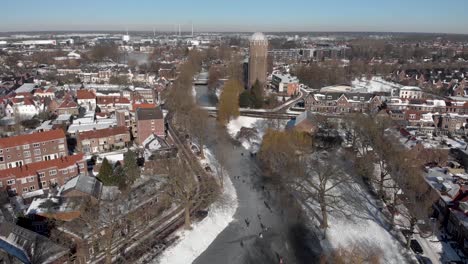antigua torre de agua escena de invierno nevada urbana aérea con gente patinando sobre hielo a lo largo del canal congelado curvo que atraviesa la ciudad holandesa de zutphen con sombras de árboles estériles arrojados sobre el hielo