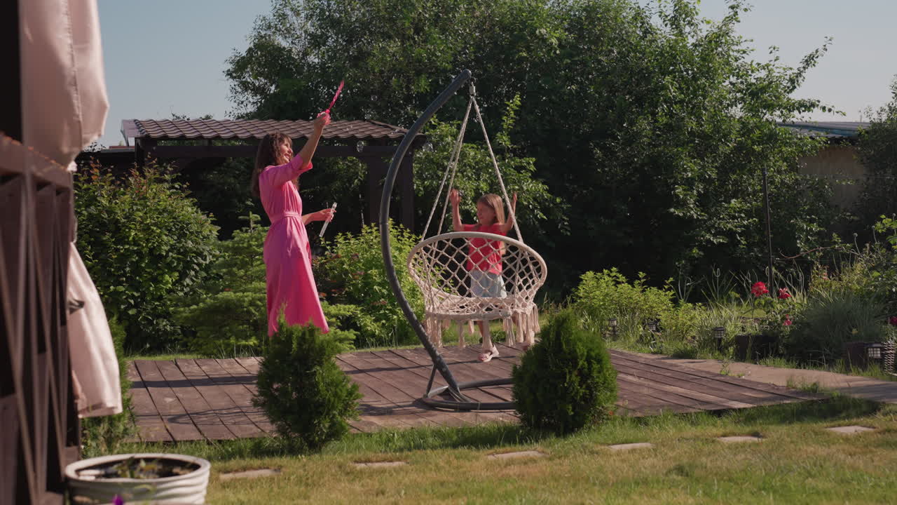 Mother Assists Daughter, Outdoor Family Fun Moment, Sunlit Garden With Parents And Kids Having Fun, Smiling Mother Guiding Her Daughter Into Swinging Seat Amidst Lush Garden Surroundings