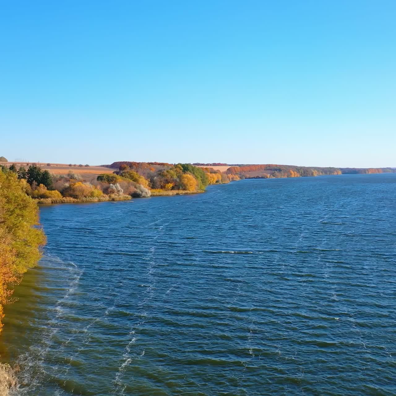 Stunning scenery of the dark blue river and colorful bank. Ripple surface of dark waters. A top view wide river and autumn forest