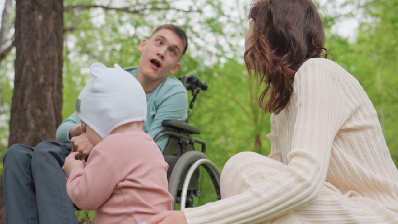 Baby Meeting Family Members Including Person In Wheelchair And Woman Caregiver In Park, Inclusive Interaction With Smiles And Gentle Reach, Accessible Outdoor Scene With Trees And Warmth